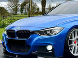 A blue BMW car is parked on a wet road, with trees and overcast skies in the background, showcasing its sleek design and prominent front headlights.