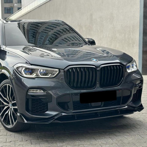 A parked, sleek, black BMW SUV with shiny alloy wheels reflects nearby buildings, positioned on a gray, paved urban surface near a modern structure.