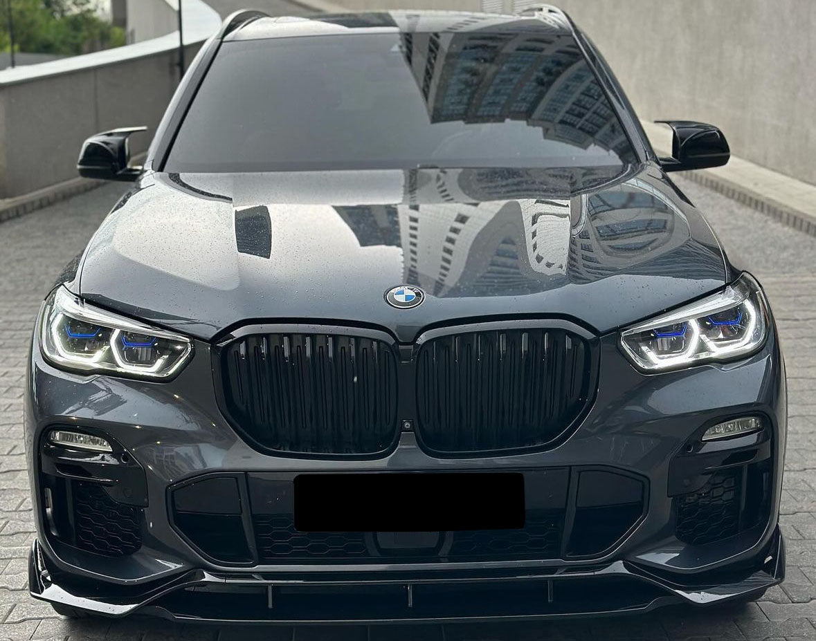 Car parked on a paved area. The sleek, black vehicle has prominent grille and headlights, with reflections of tall buildings on its glossy surface. The environment appears urban and modern.