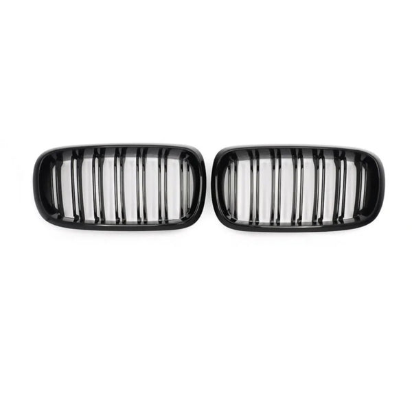 Two black car grilles, each with vertical slats, are positioned side by side against a plain white background.