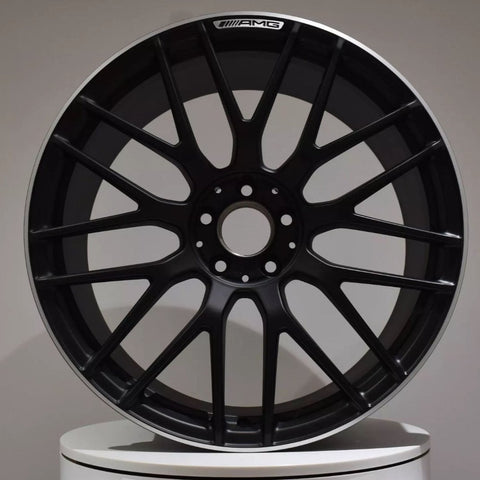A black AMG car wheel rim with a multi-spoke design is displayed against a plain background, positioned upright on a circular white platform.