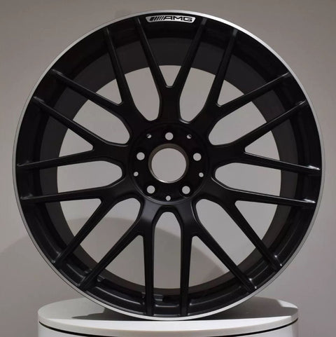 A black car wheel with multiple spokes displays the "AMG" logo at the top, set against a plain gray background on a white surface.