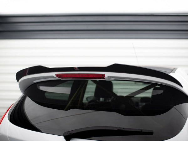 A white car's rear hatch with a black spoiler, featuring a centered red brake light, is parked in front of a white garage door with horizontal panels.