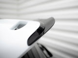 A sleek black and white car spoiler is attached to a vehicle, shown close-up. It's positioned in a brightly lit area with blurred, light-colored background lines.