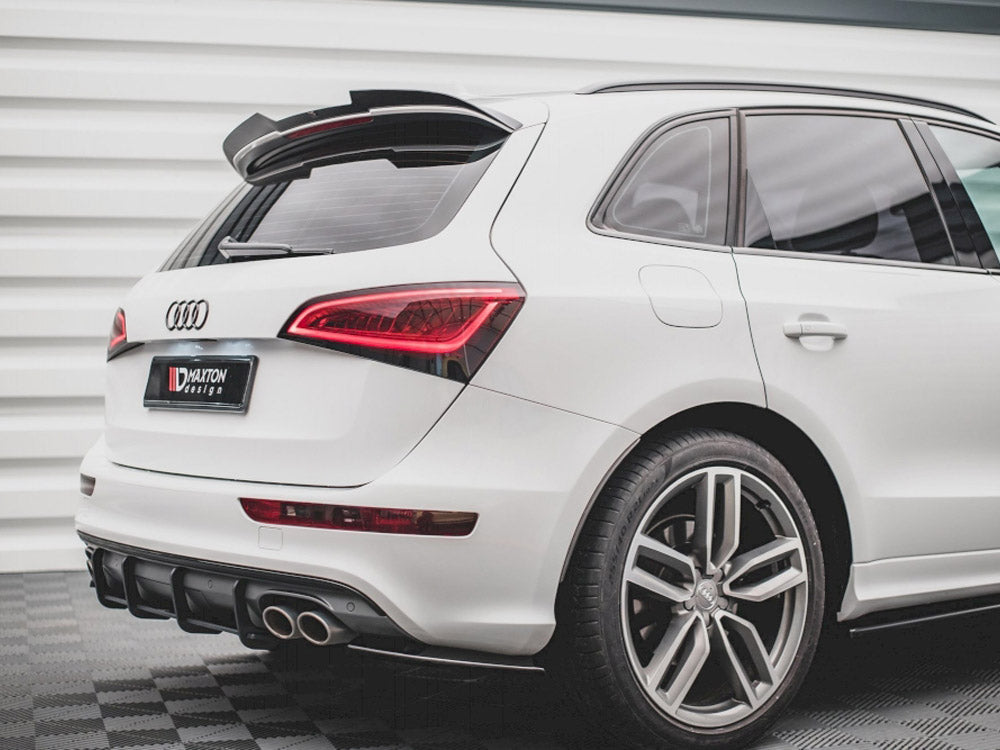 A white Audi SUV is parked on a checkered floor, featuring a prominent rear spoiler and dual exhaust pipes. Text on a license plate reads "Maxton Design."