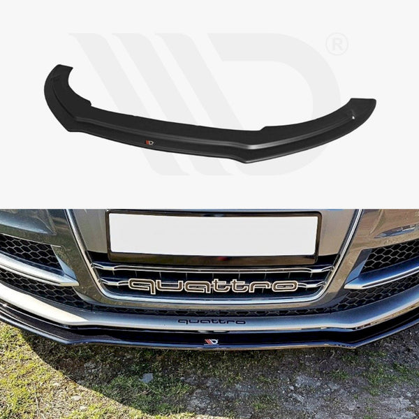 A black front lip spoiler, positioned above a car's bumper, labeled "quattro." The car is parked on grass, showcasing its detailed grille and daytime running lights.