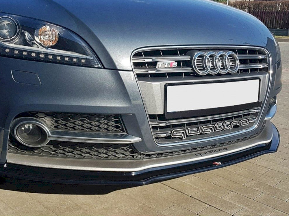 The image shows the front bumper of an Audi car with "TTS" and "quattro" logos. The vehicle is parked on a paved surface with a clear sky above.