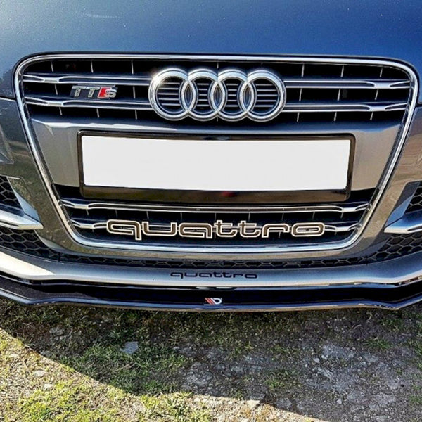 Car front features Audi grille with four rings, "TT RS" badge, "quattro" text, and blank license plate. Positioned over grass and gravel on a sunny day.