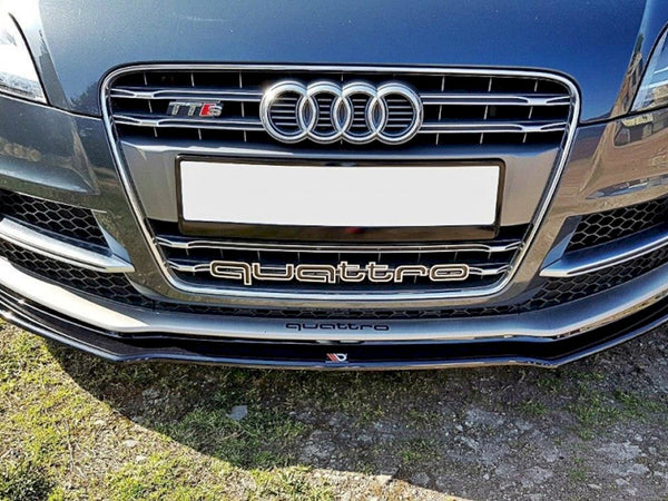 Car front features Audi grille with four rings, "TT RS" badge, "quattro" text, and blank license plate. Positioned over grass and gravel on a sunny day.