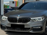A sleek, gray sedan is parked at a gas station, showcasing its distinctive front grille and headlights. The background includes fuel pumps and a building.