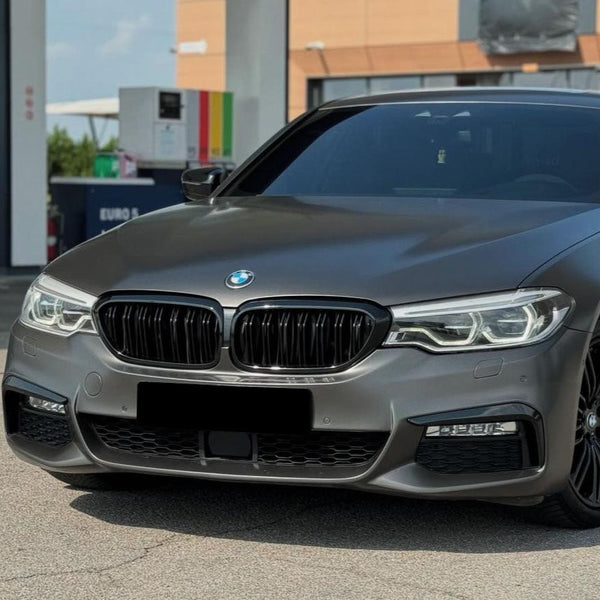 A sleek, gray sedan is parked at a gas station, showcasing its distinctive front grille and headlights. The background includes fuel pumps and a building.