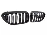 Two glossy black car grilles, featuring vertical slats, are positioned against a plain white background, highlighting their sleek and modern design.