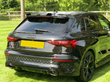 A black Audi car is parked on a grassy area surrounded by trees and a wooden fence. It has prominent dual exhaust pipes and tinted windows.