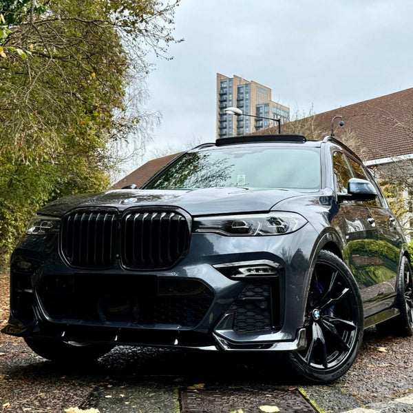 A sleek, black SUV is parked on a wet, leaf-covered road, surrounded by trees and buildings in the background, under a cloudy sky.