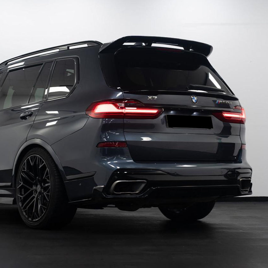 An SUV, stationary, is shown from the rear with illuminated taillights. The model is labeled "BMW X7 M50d." Its dark color contrasts against a bright, indoor background.
