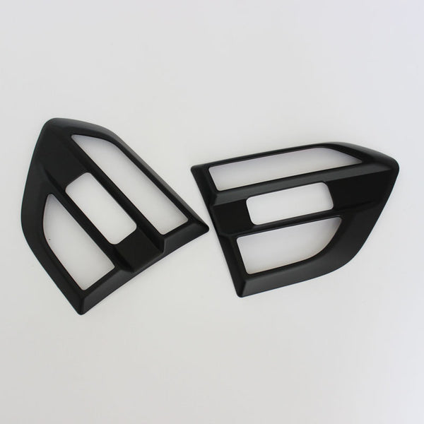 Two black plastic car components, resembling air vent covers, lie side by side on a white surface, showcasing a glossy finish and geometric cutouts.