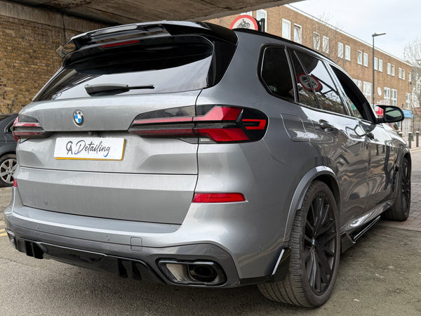 A silver BMW SUV is parked under a bridge, displaying "A Detailing" on the license plate. Nearby, brick buildings and street signs are visible in an urban setting.