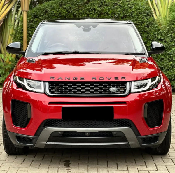 A red Range Rover is parked on a brick driveway, surrounded by lush greenery. The front of the car prominently displays the "RANGE ROVER" and "LAND ROVER" logos.