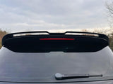A car with a rear window featuring a wiper and a spoiler, surrounded by overcast skies and leafless trees.