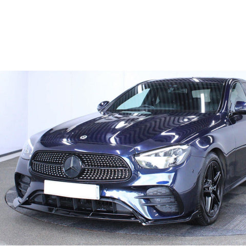 A sleek, dark blue Mercedes-Benz car is parked in a well-lit indoor space, featuring a prominent front grille and modern headlights, with reflective surfaces highlighting its polished finish.