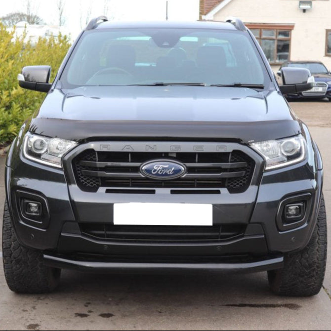 A black Ford Ranger parked on a driveway, featuring a prominent grille with "RANGER" text. In the background, there’s a house, trees, and another parked car.