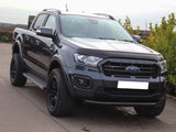 A dark gray Ford Ranger pickup truck is parked on a concrete driveway, surrounded by green foliage and a clear sky.