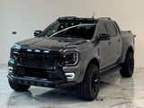 A dark gray pickup truck with rugged tires and LED lights is parked indoors on a polished tiled floor, under bright overhead lighting, showcasing a modern design.