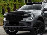 A grey pickup truck with a rugged front grill and blacked-out wheels is parked in front of a building with lush, green ivy covering its walls.