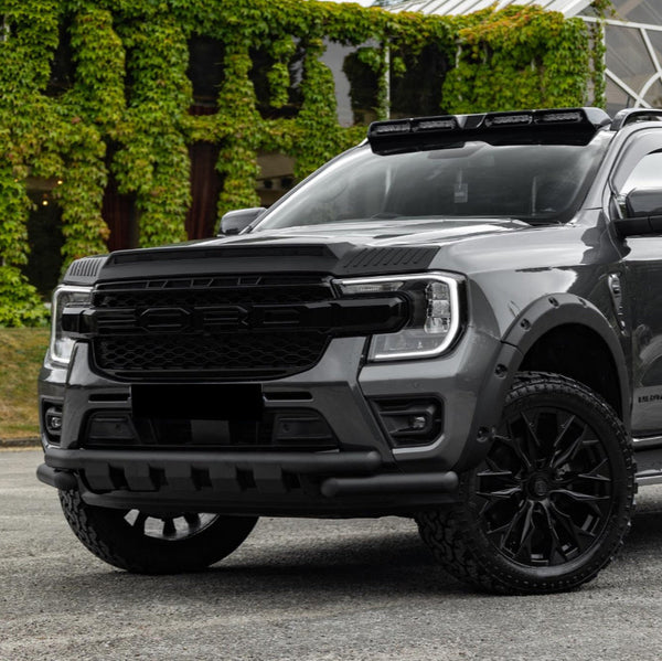 A grey pickup truck with a rugged front grill and blacked-out wheels is parked in front of a building with lush, green ivy covering its walls.