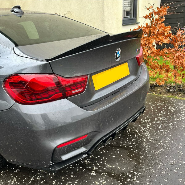 A gray BMW car is parked with rain droplets on its surface, surrounded by wet pavement and orange leaves. The license plate is yellow and blank.