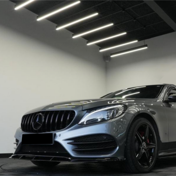 A sleek, silver car sits stationary, illuminated by bright ceiling lights in a modern showroom. The car features black alloy wheels and a prominently displayed logo on the grille.