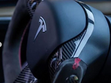 A sleek steering wheel with a Tesla logo, featuring carbon fiber detailing, situated in a modern car interior with soft lighting.