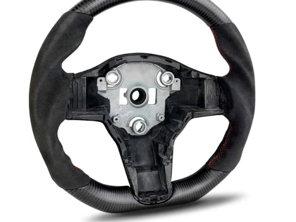 A carbon fiber steering wheel with a central metal hub is positioned upright. It features red stitching and lacks controls, set against a plain white background.