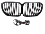 A black car grille with vertical slats is positioned above a coiled set of black electrical cables, both set against a plain white background.