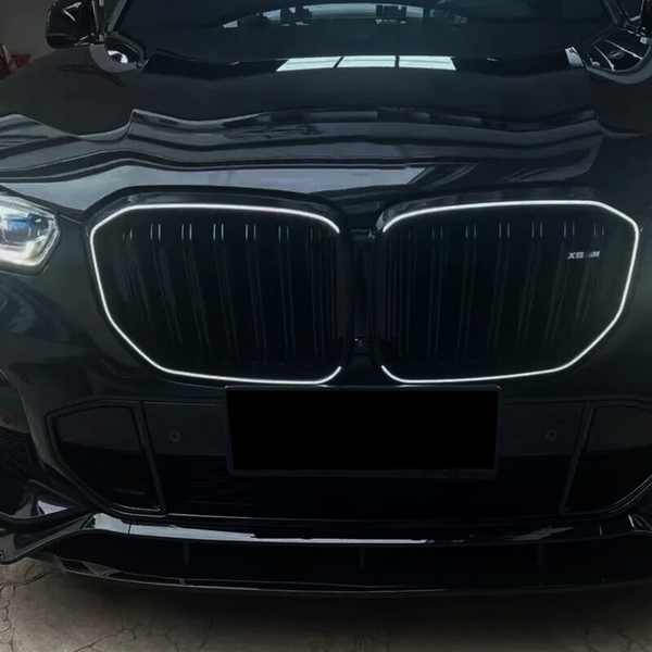A black car with a prominent, illuminated grille, showcasing a sleek design. The front is parked indoors, with reflections visible on the shiny surface. "X5 M" is marked on the grille.