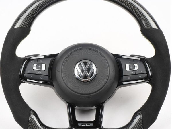Steering wheel with carbon fiber accents and VW logo, featuring multi-function buttons for control. It rests against a plain white background.