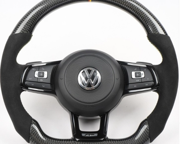 Steering wheel with carbon fiber accents and VW logo, featuring multi-function buttons for control. It rests against a plain white background.