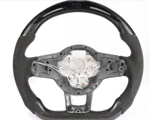 A steering wheel, partially covered in carbon fiber and black suede, has exposed wiring and a metal frame in the center, set against a plain white background.