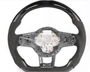 A steering wheel, partially covered in carbon fiber and black suede, has exposed wiring and a metal frame in the center, set against a plain white background.