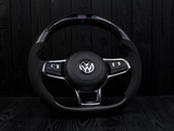 A Volkswagen steering wheel sits upright, displaying buttons on its arms, against a dark wooden background.