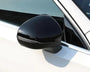 A black side mirror is attached to a white car, reflecting light in a sunny outdoor setting. The vehicle's window and frame are partially visible.