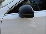 A black side mirror is attached to the passenger side of a white car, reflecting nearby trees and sky in a parking lot setting.
