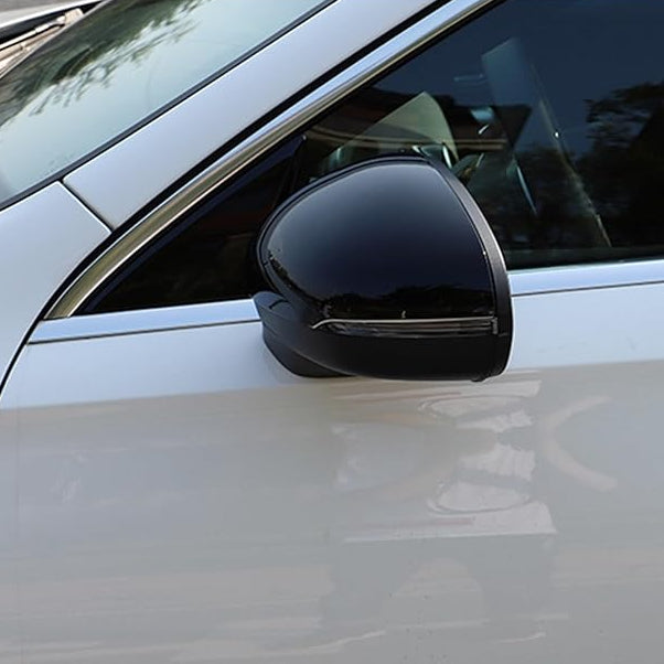 A black side mirror is attached to the passenger side of a white car, reflecting nearby trees and sky in a parking lot setting.