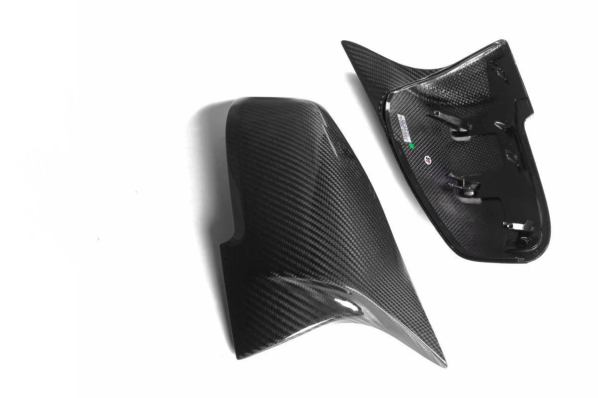 Two glossy carbon fiber car mirror covers, one showing reflective surface, other displaying interior fittings, placed on a plain white background.