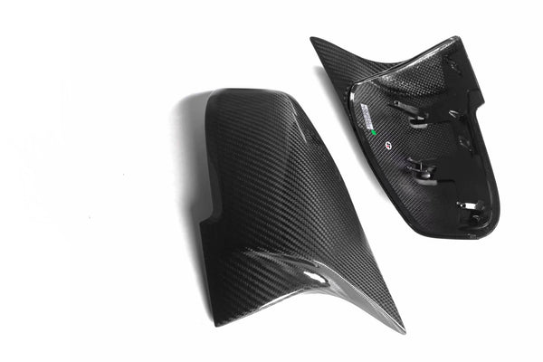 Two glossy carbon fiber car mirror covers, one showing reflective surface, other displaying interior fittings, placed on a plain white background.