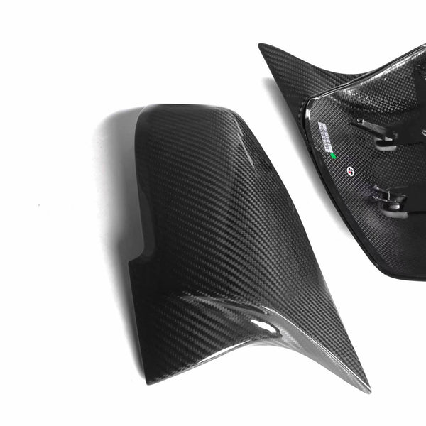Two carbon fiber car mirror covers rest side by side on a white surface. The right cover shows the interior structure with mounting clips visible.