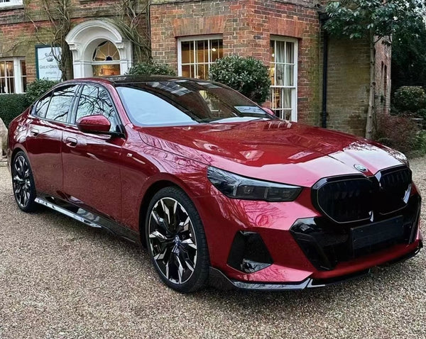 A sleek red car, parked stationary, is in front of a brick building with vines. The building has white-framed windows and a sign reading "Great Gransden Antiques."