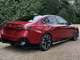 A red BMW 530e is parked on a gravel surface, surrounded by lush greenery. The car's sleek design and shiny wheels stand out.