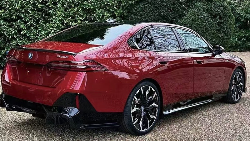 A red BMW 530e is parked on a gravel surface, surrounded by lush greenery. The car's sleek design and shiny wheels stand out.
