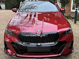 A red BMW car is parked on a gravel driveway, reflecting tree branches on its polished surface, with a brick building and greenery surrounding it.